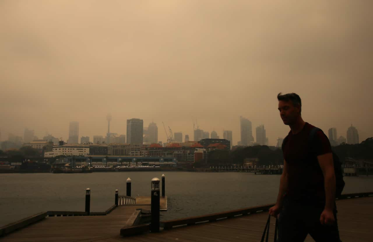A man walks long the foreshore in Blackwattle bay as smoke haze from bushfires in New South Wales blankets the CBD in Sydney, Tuesday, December 10, 2019. (AAP Image/Steven Saphore) NO ARCHIVING