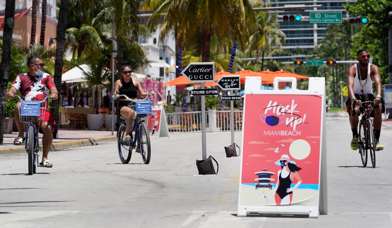 Bike riders ride past a Mask Up Miami Beach, sign on Florida's famed Ocean Drive.
