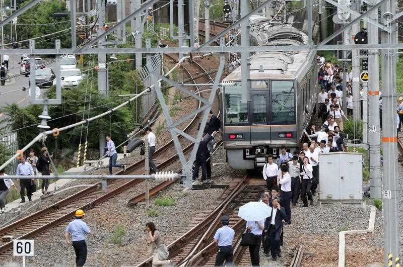 Passengers on board a commuter train walk on the railway due to suspended service, after a magnitude 6.1 earthquake hit western Japan, in Osaka, 18 June 2018.