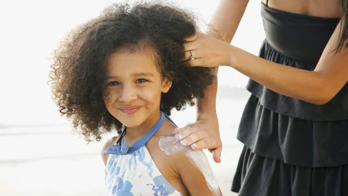 Hispanic mother rubbing sunscreen on daughter at beach