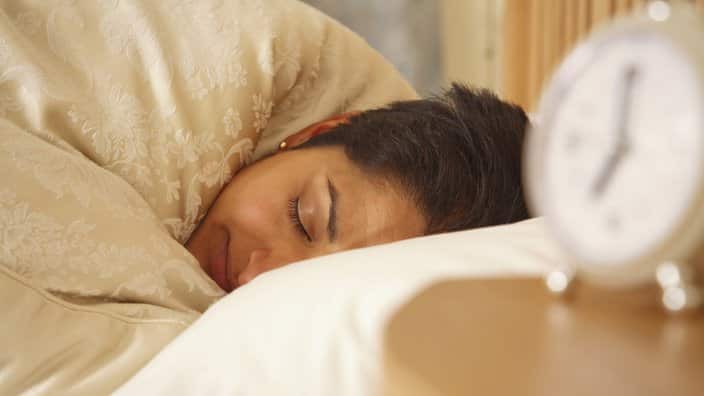 Young Indian woman sleeping in a bed with an alarm clock in the foreground