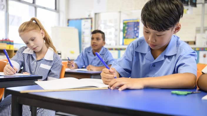 Multi racial school children sitting at their desks and writing in books