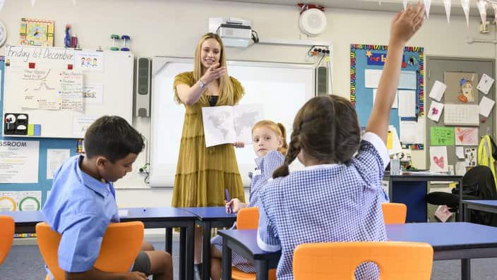 Young primary school teacher pointing at girl with arm raised in classroom