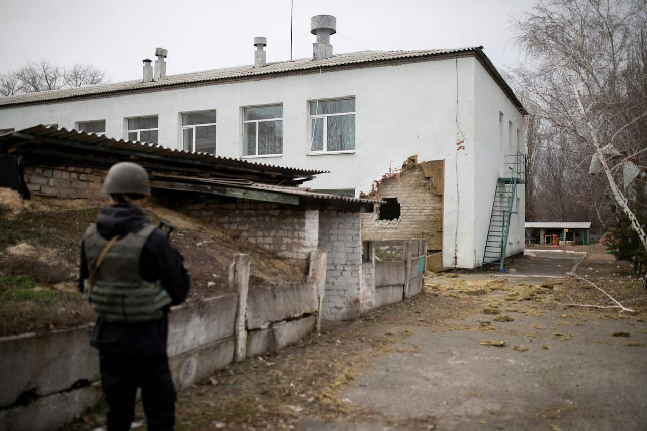 A Ukrainian soldier stands next to a damaged wall after the reported shelling of a kindergarten in the settlement of Stanytsia Luhanska.