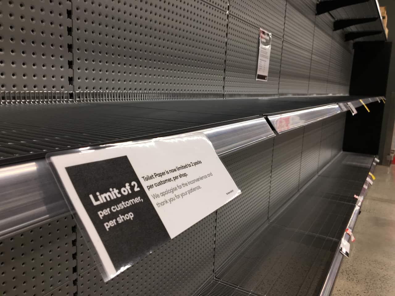 Signage for product limits is seen on an empty toilet paper shelf in a Woolworths supermarket in Melbourne.