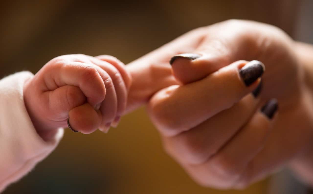 A baby holding the finger of its mother