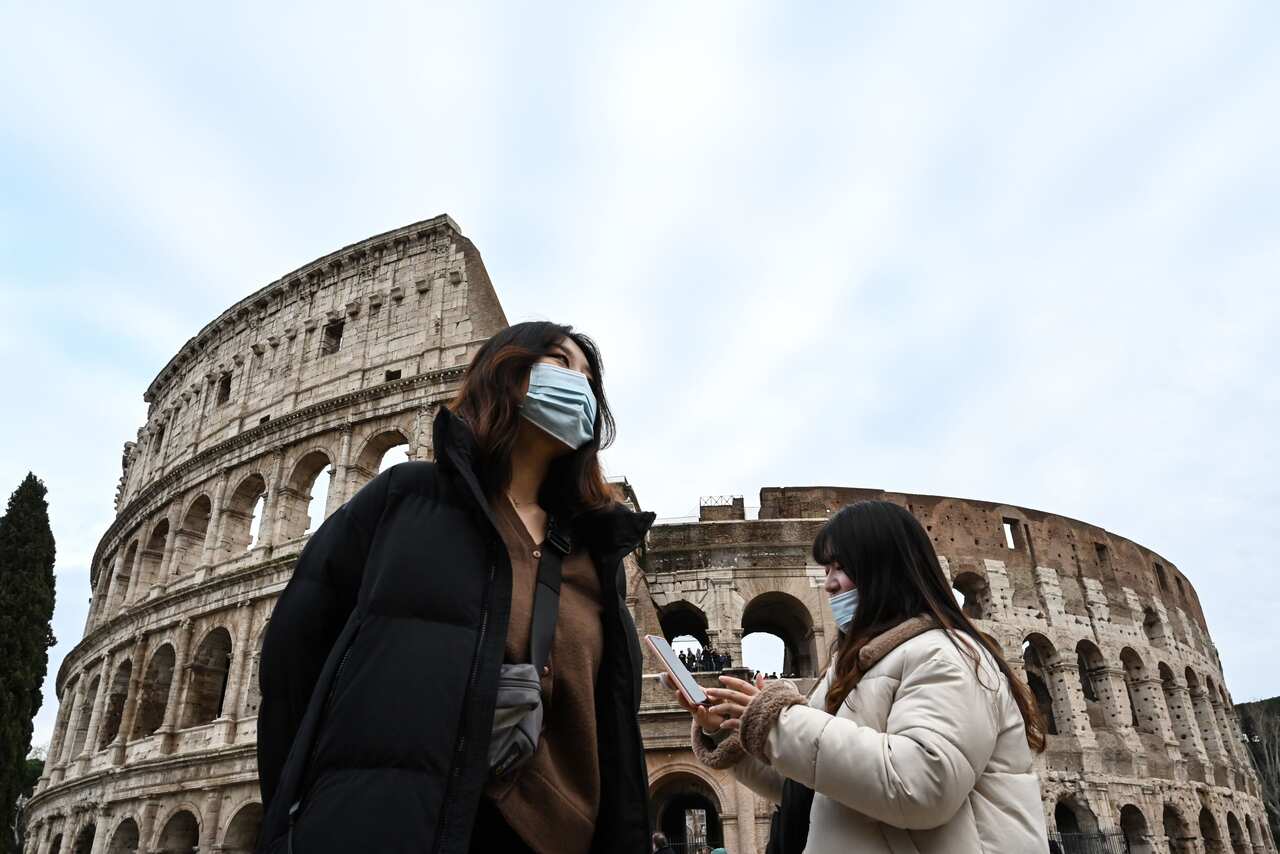Tourists wearing protective respiratory masks tour downtown Rome.