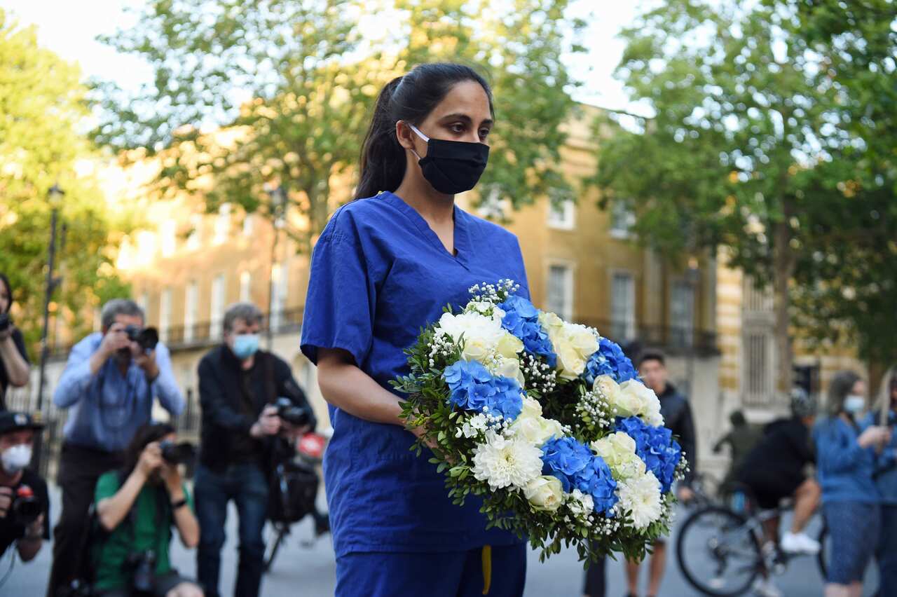 A woman wearing medical scrubs and a black mask carries a wreath of flowers in memory of people who have died during the coronavirus pandemic in the UK.