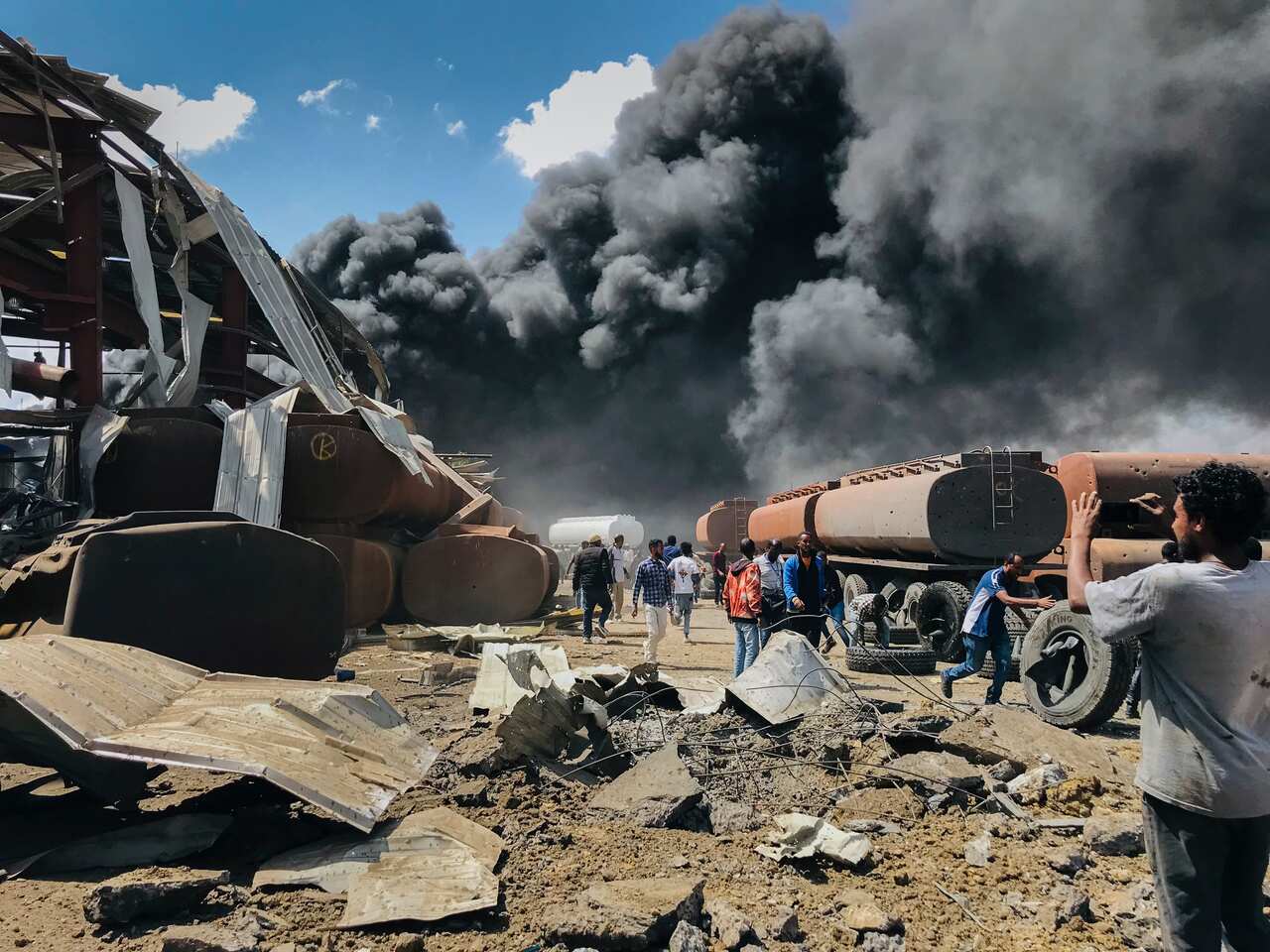 People are seen in front of clouds of black smoke from fires in the aftermath at the scene of an airstrike in Mekele, the capital of the Tigray region in 2021.