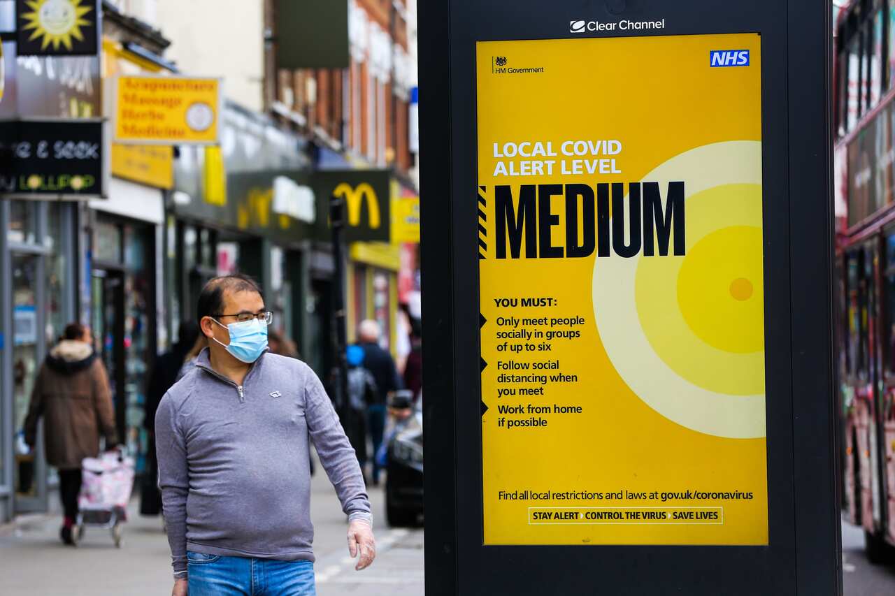 A man wearing a face mask walks past a public information poster in London, as the capital moves to tier two restrictions.