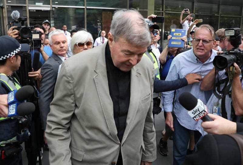 Pell pushes through the media pack outside court.