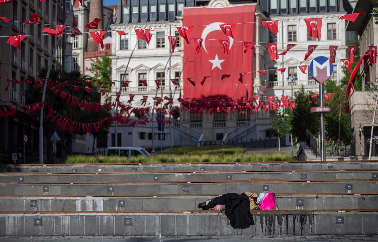 A homeless woman sleeps in front of the huge Turkish flag during a curfew amid the ongoing pandemic of COVID-19.