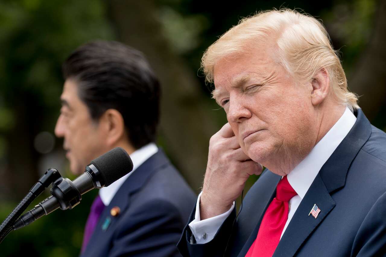 President Donald Trump puts in an earpiece for translation as Japanese Prime Minister Shinzo Abe, left, speaks at a news conference