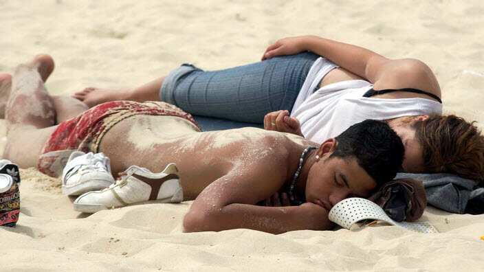 An empty can of alchohol lays near two schoolies asleep on the beach after a night of partying