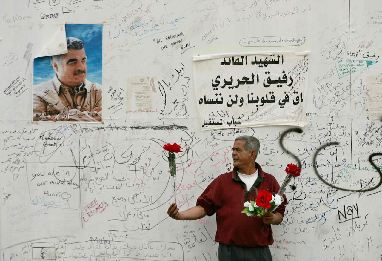 A Lebanese vendor sells plastic flowers in front of a poster of slain former Prime Minister Rafiq Hariri signed by supporters near Haririi's gravesite in Martyr's Square, central Beirut, Lebanon