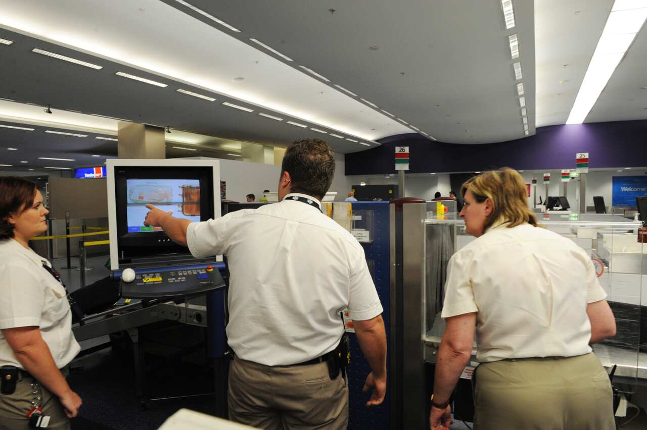 Quarantine Inspection Service officers use an x-ray machine to search passenger bags for fruit and other prohibited items at Sydney 