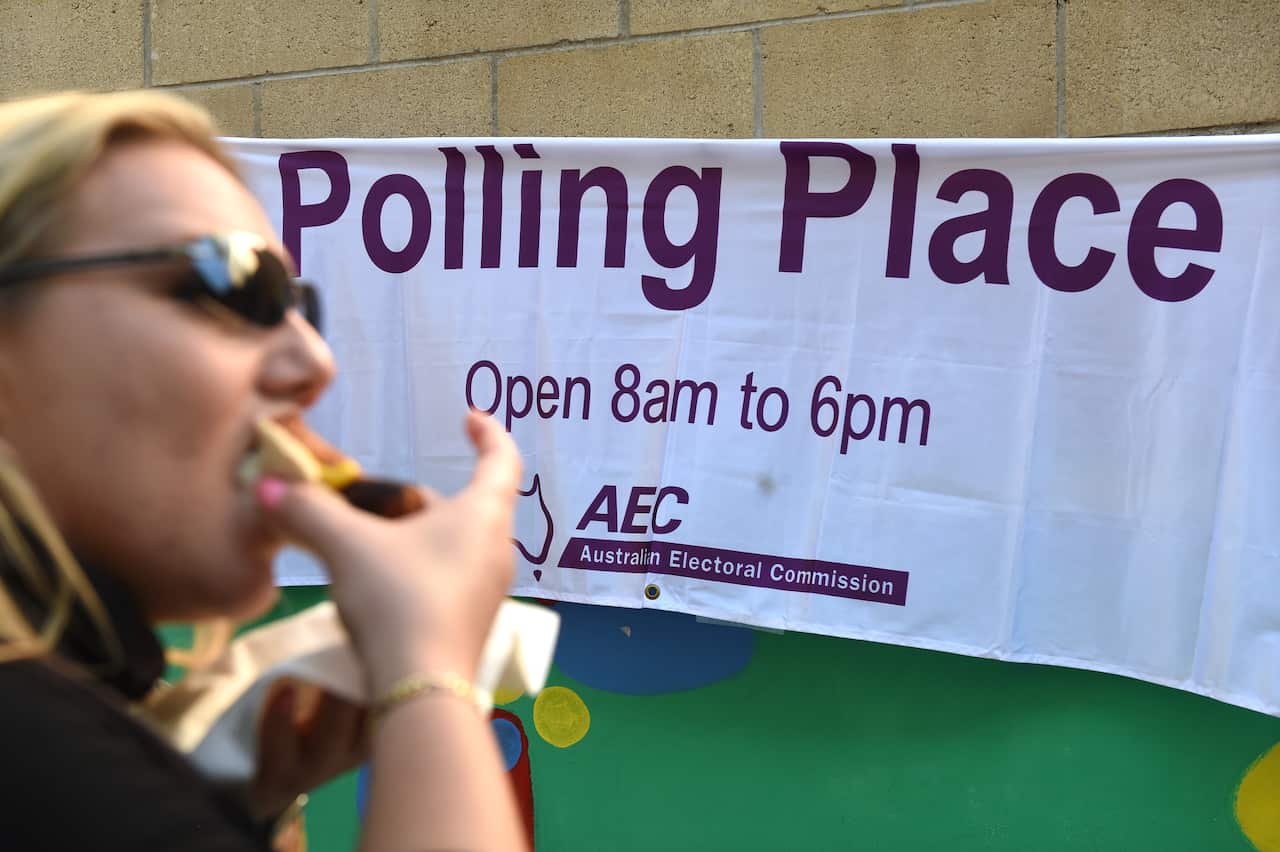 A voter eats a sausage as she lines up to cast her ballot in Brisbane, Saturday, July 2, 2016. About 15 million Australians will vote in today's federal election. (AAP Image/Dan Peled) NO ARCHIVING