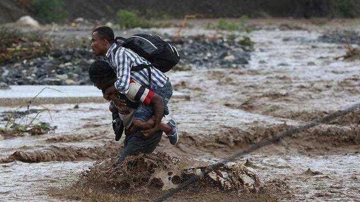 People cross a flooded street after the passing of hurricane Matthew in the country, in Grand Goave, Haiti.)