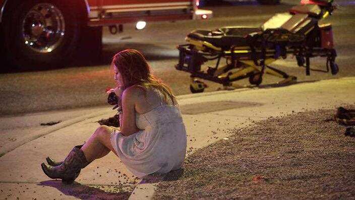 A woman sits on a curb at the scene of a shooting outside of a music festival along the Las Vegas Strip, Monday, Oct. 2, 2017, in Las Vegas.