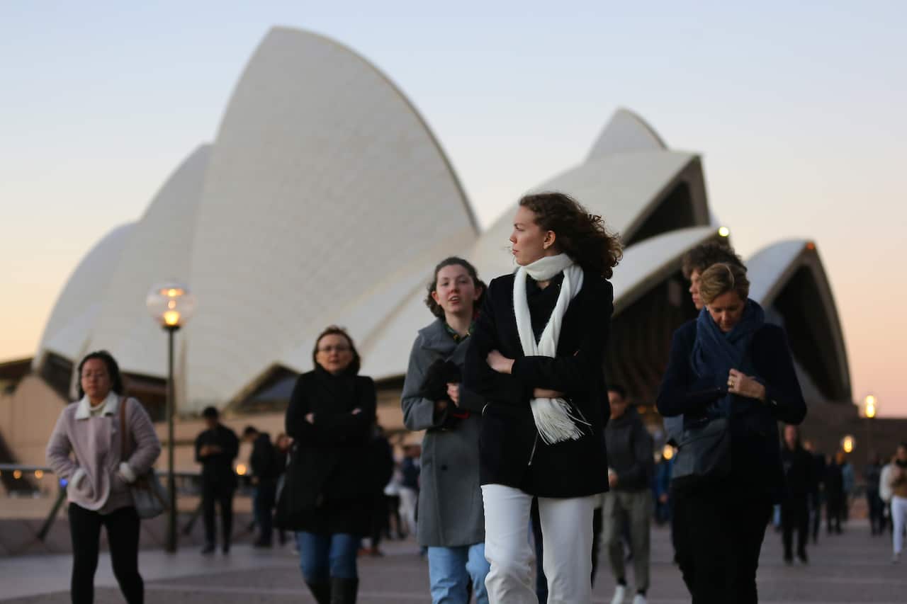 People walk in front of the Sydney Opera House during windy weather in Sydney, Saturday, July 13, 2019. (AAP Image/Steven Saphore) NO ARCHIVING