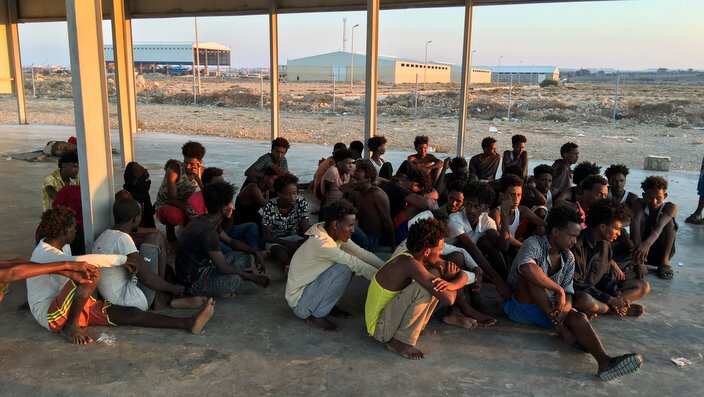 Rescued migrants sit on a coast some 100 kilometers (60 miles) east of Tripol