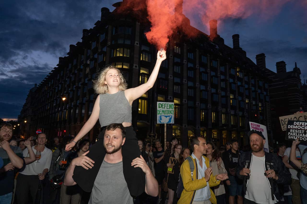 A woman is seen with a flare on westminster bridge outside the houses of parliament where hundreds of people are seen protesting against Boris Johnson.
