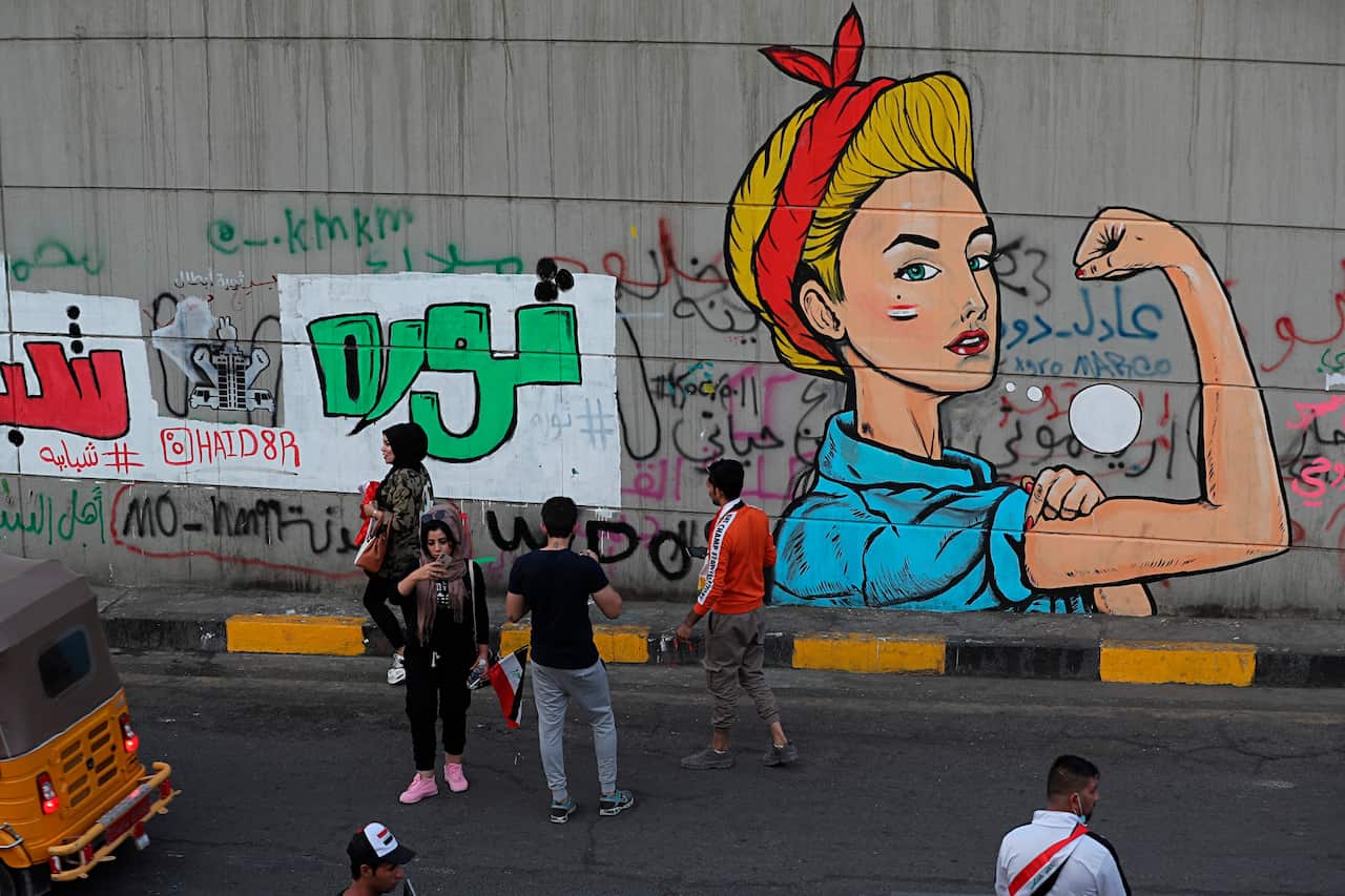 Anti-government protesters stand near graffiti messages in Arabic, including "Youth Revolution" near Tahrir Square during ongoing protests in Baghdad, Iraq, Sunday, Nov. 3, 2019. (AP Photo/Khalid Mohammed)