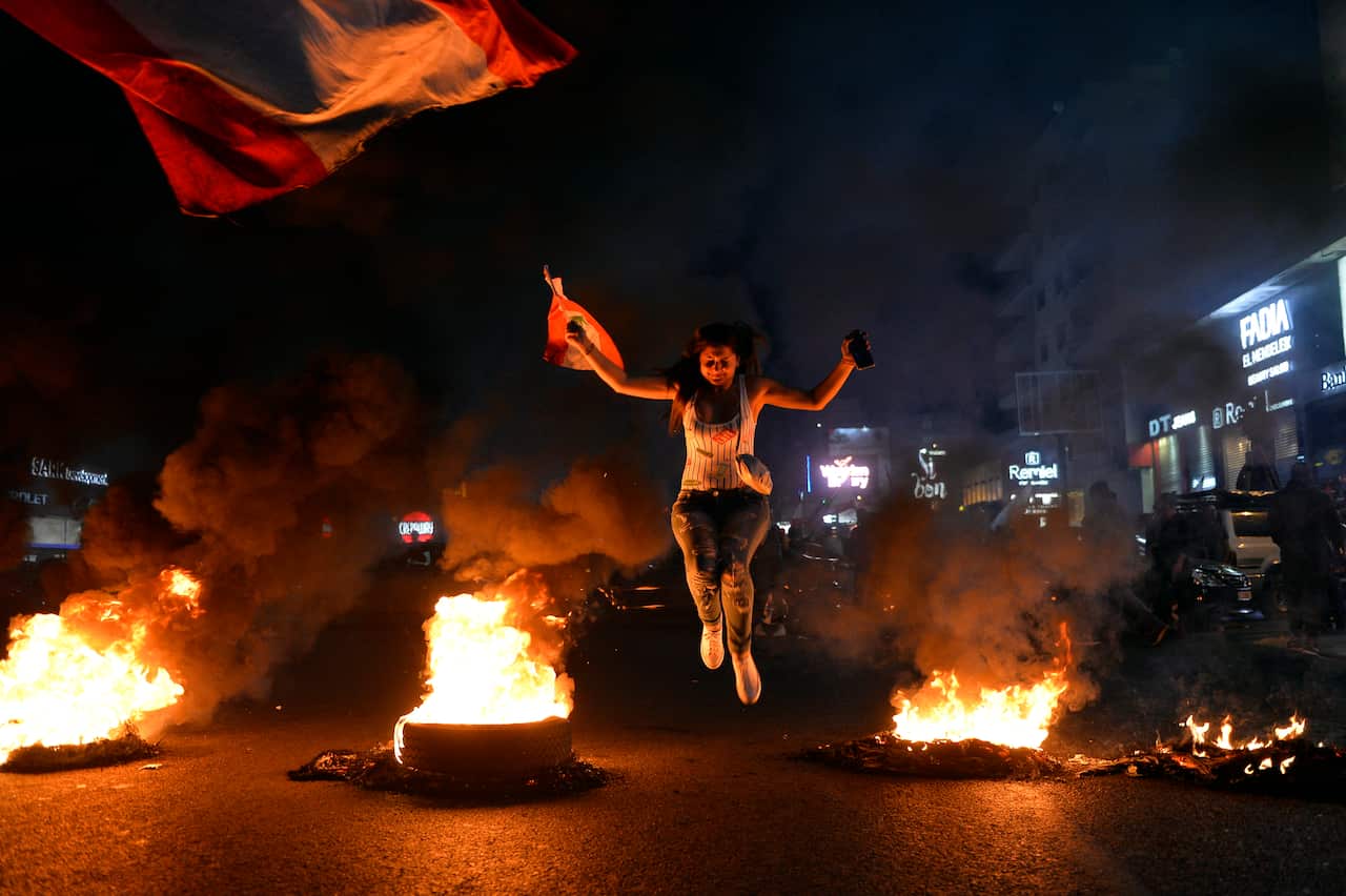 A protester jumps over burning tires as other protesters block the main highway during a protest at Zalka north of Beirut