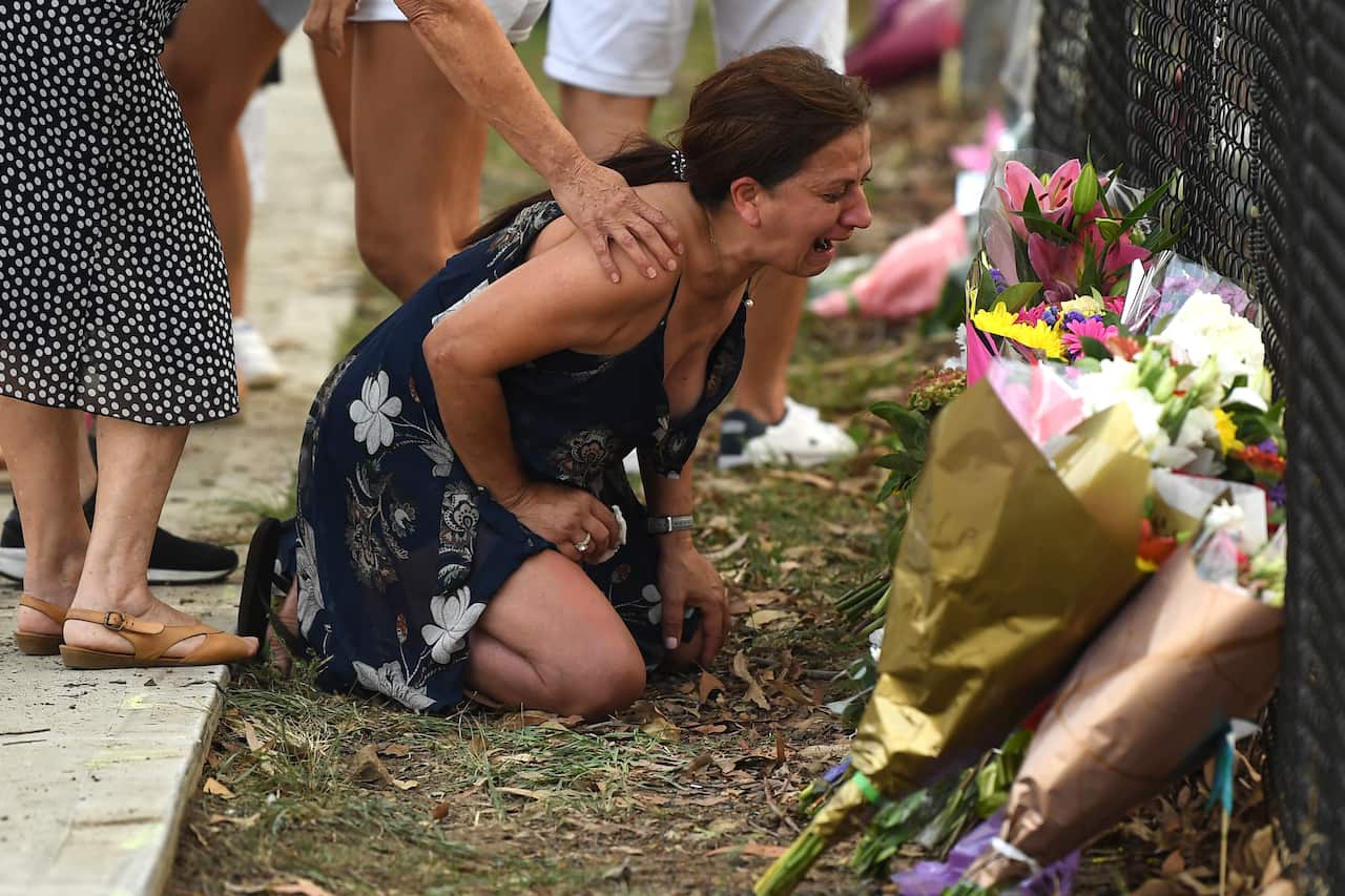 A woman pauses near flowers placed at the scene where seven children where hit on a footpath by a four-wheel drive in the Sydney suburb of Oatlands