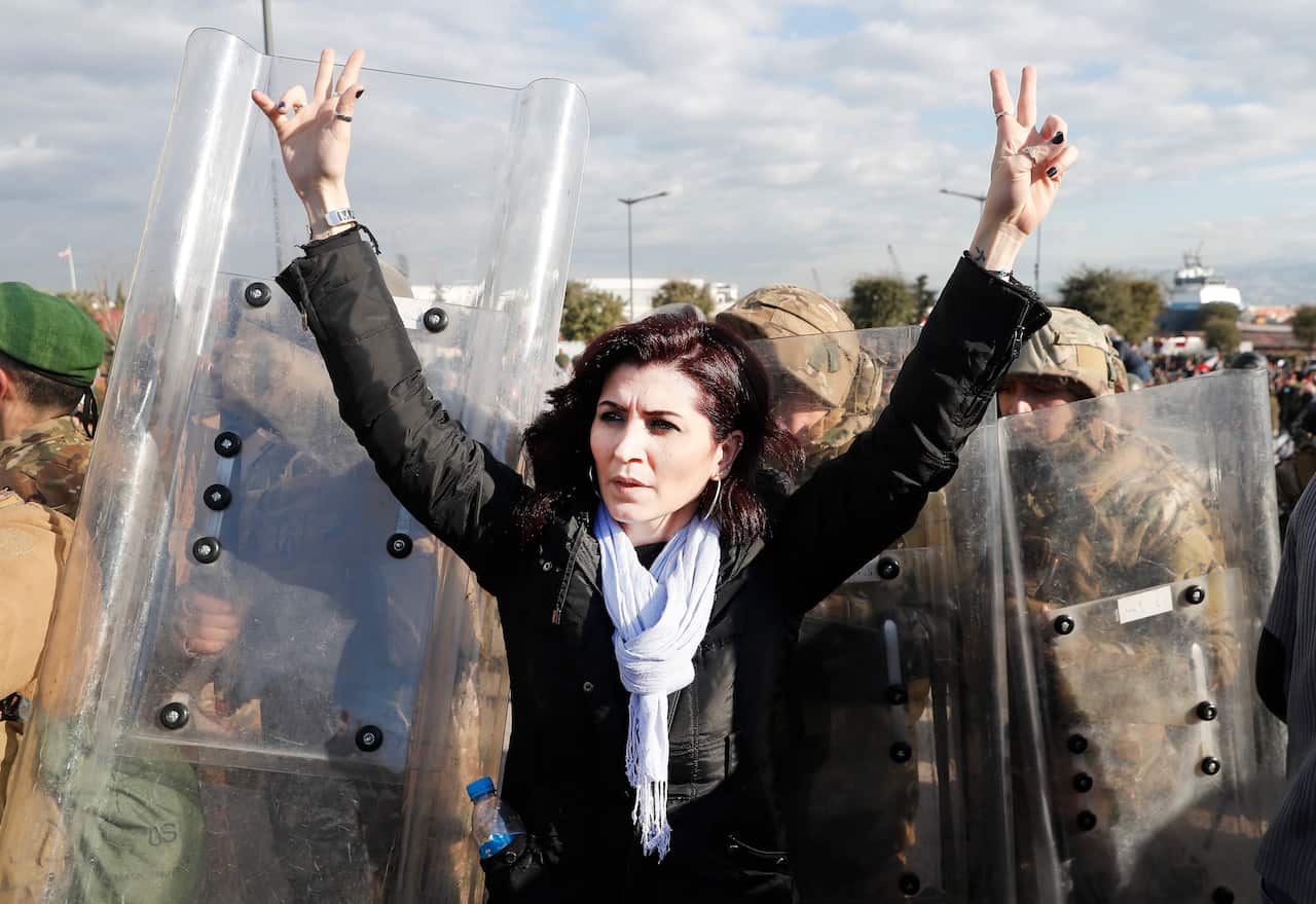 An anti-government protester flashes victory signs as she stands in front of army soldiers during a protest in downtown Beirut, Lebanon,Tuesday, Feb. 11, 2020. (AP Photo/Hussein Malla)