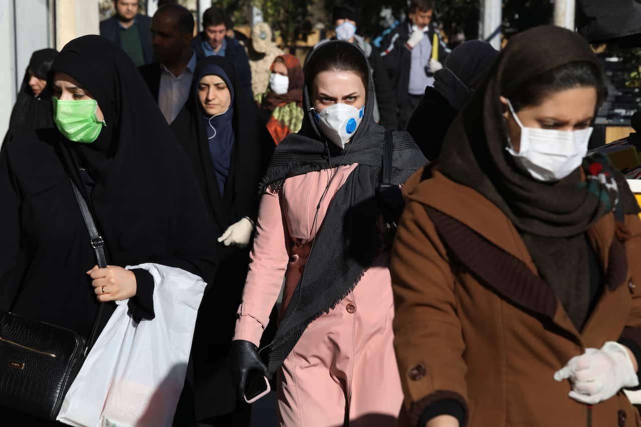 People wearing face masks walk on a sidewalk in downtown Tehran, Iran, Monday, March 2, 2020.