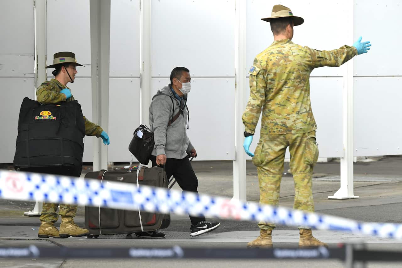 the Defence Force watches over as returning overseas travellers are ushered towards waiting busses for the beginning of their 14-day imposed quarantine 