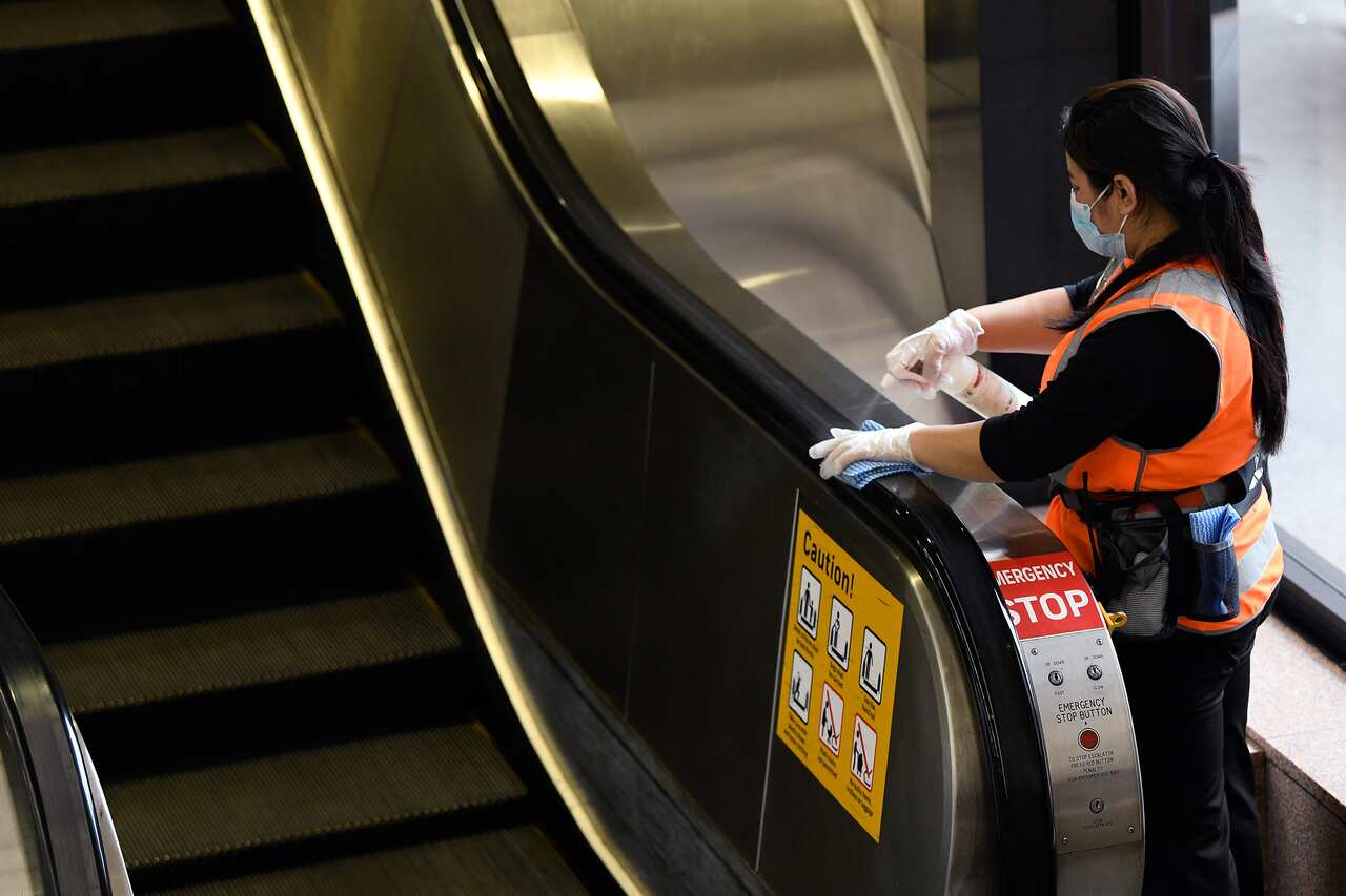 A cleaner wearing a face mask and gloves cleans the railing on the escalator at Circular Quay