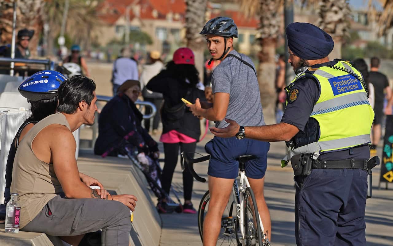 Victoria Police officer speak to a man at St Kilda beach, Melbourne, April 13, 2020 amid Covid-19 social distancing measures.