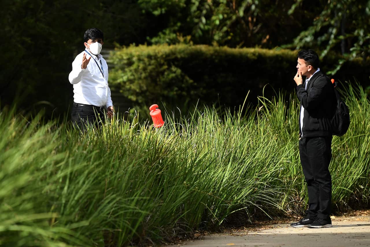 A security guard speaks with a worker leaving the Anglicare Newmarch House in Western Sydney, Sunday, April 26, 2020. NSW's COVID-19 death toll now stands at 36 after a sixth resident died at the aged care home where almost 50 people have been infected. 