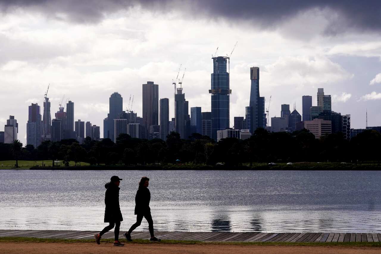 People walk around Albert Park Lake as storm clouds hover over the city skyline in Melbourne.
