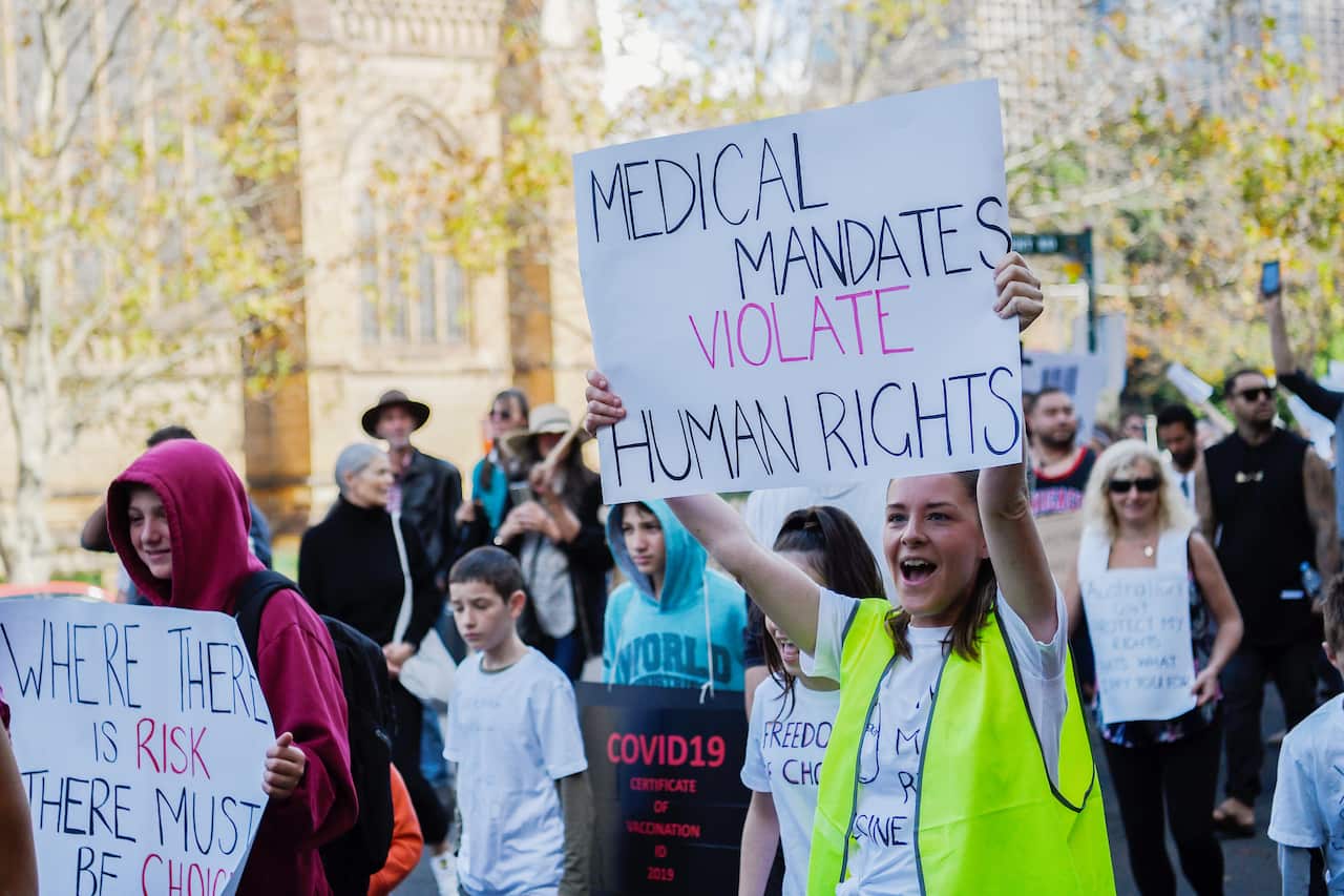 Protestors are seen holding placards during the 'Wake Up Australia!' march against mandatory vaccinations at Hyde Park in Sydney, Saturday, May 30, 2020. (AAP Image/Bianca De Marchi) NO ARCHIVING