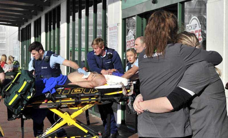Supermarket staff embrace as police officers take a victim to an ambulance outside a Countdown supermarket in central Dunedin, New Zealand, Monday May 10, 2021.