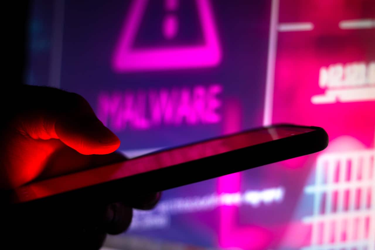 In this photo illustration the malware logo seen in the background of a silhouette hand holding a mobile phone. (Photo by Rafael Henrique / SOPA Images/Sipa USA)