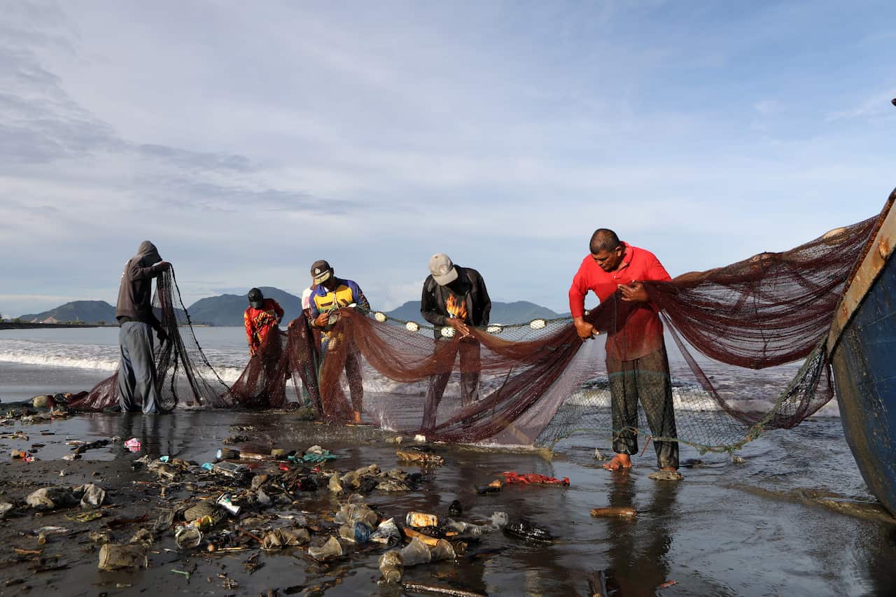 Fishermen clean their net from the plastic garbage washed ashore at Banda Aceh, Indonesia.