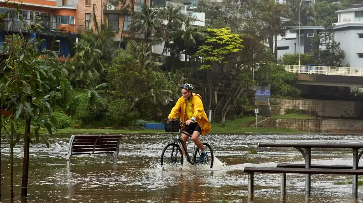 A bike rider is seen riding the flooded footpath at Manly Lagoon. 