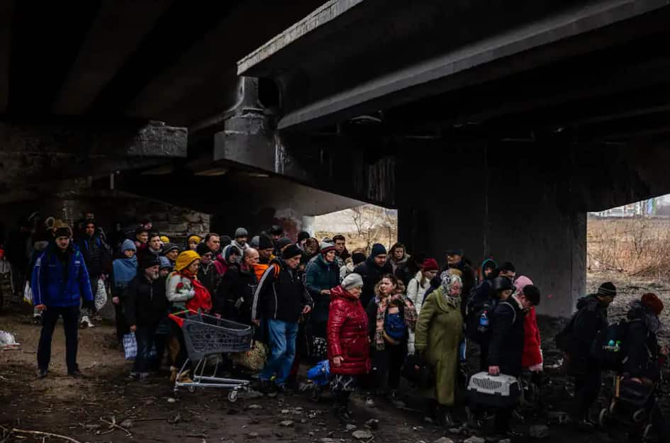 Evacuees stand under a destroyed bridge as they flee the city of Irpin, northwest of Kyiv, on 7 March 7, 2022