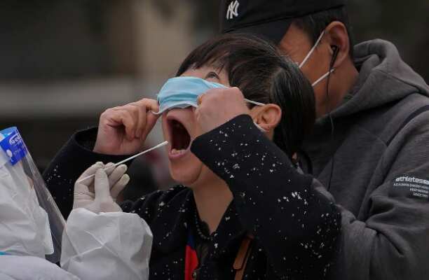 A woman pulls up her mask to get her throat swab at a coronavirus testing site near residential buildings on Wednesday, 6 April, 2022, in Beijing. 
