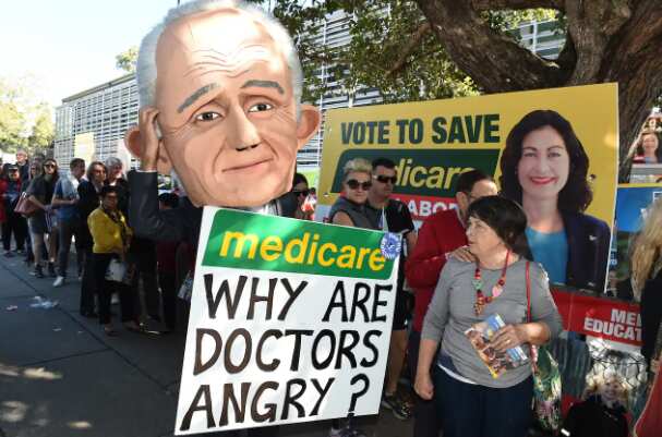 A protester wearing a giant puppet head depicting Prime Minister Malcolm Turnbull holds a sign criticising the government's policy on Medicare outside a polling booth in 2016.
