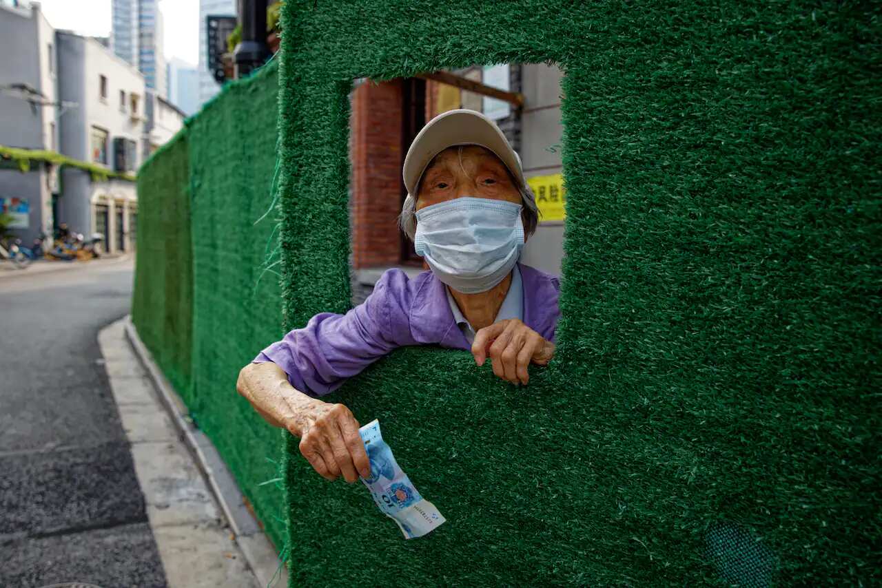 A woman asks people passing-by to buy her food through the opening in quarantine barrier, in Shanghai.