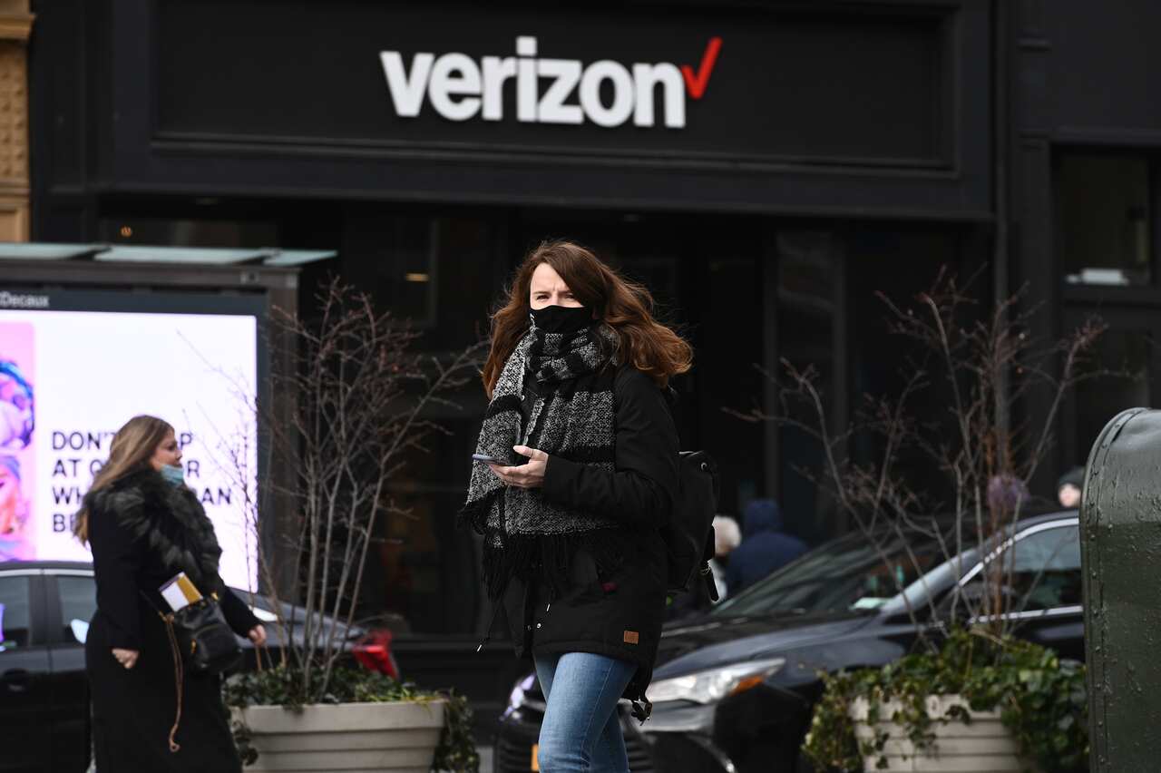 A woman holds a cell phone as she walks past a Verizon retail store in New New York, NY,