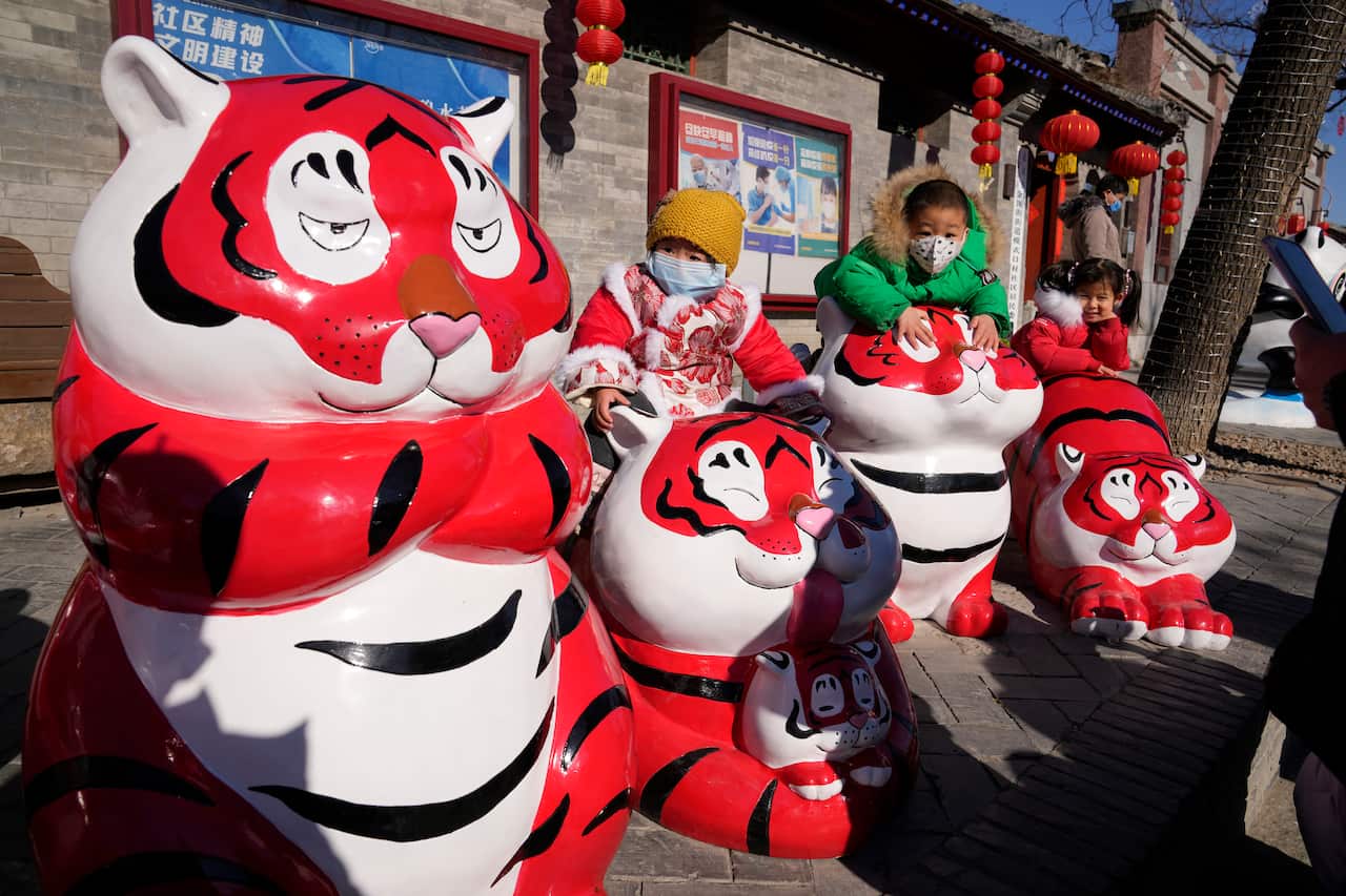 Children wearing masks pose for photos near Tiger sculptures on the first day of the Chinese Lunar Year of the Tiger in Beijing, China, Tuesday, Feb. 1, 2022. (AP Photo/Ng Han Guan)