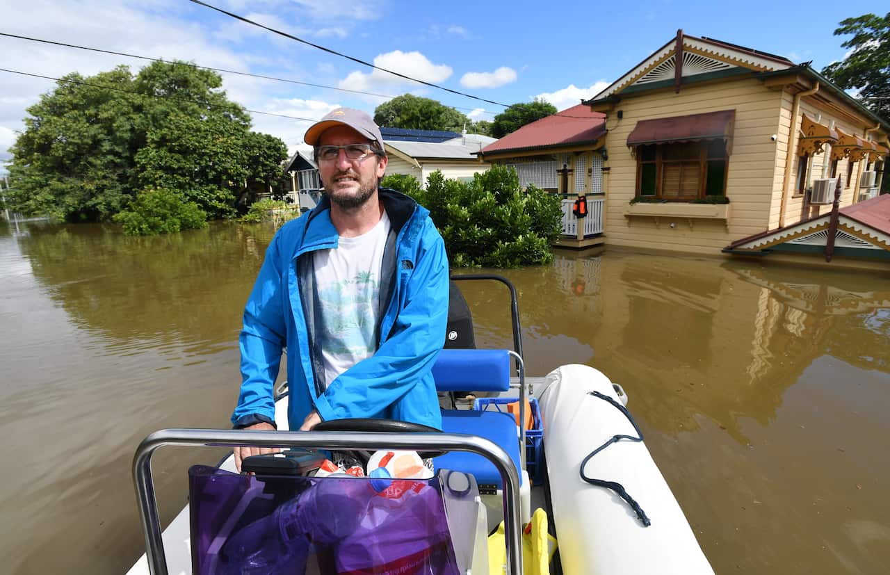 Auchenflower resident David Miller is seen navigating his boat along the street past flooded houses in the suburb of Auchenflower in Brisbane