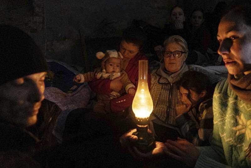 People sit around a lamp in a bomb shelter in Mariupol, Ukraine