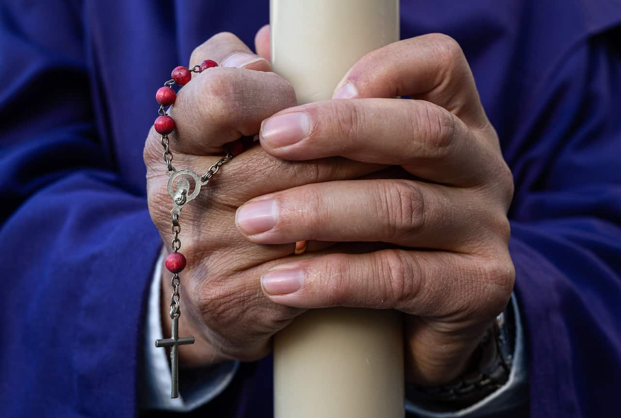 A penitent holds a candle and a rosary during a procession as they celebrate Holy Tuesday in Spain.. 